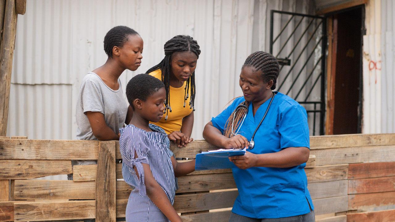 Three girls stand looking at a tablet held by a female doctor in South Africa