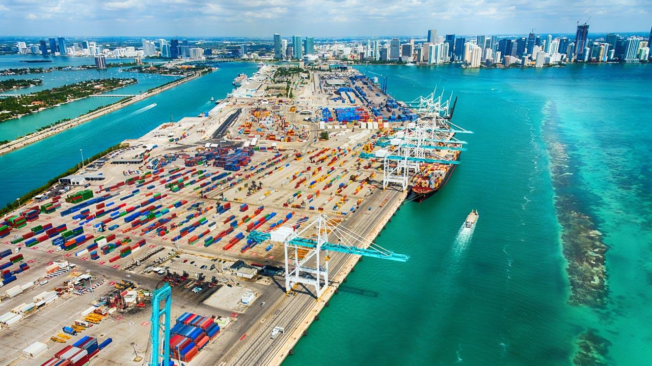 A wide-angle aerial view of the Port of Miami and Biscayne Bay, with the Miami skyline in the background